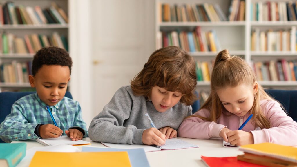 Attentive multiracial schoolkids boys and girl writing test, sitting at desk in classroom at primary