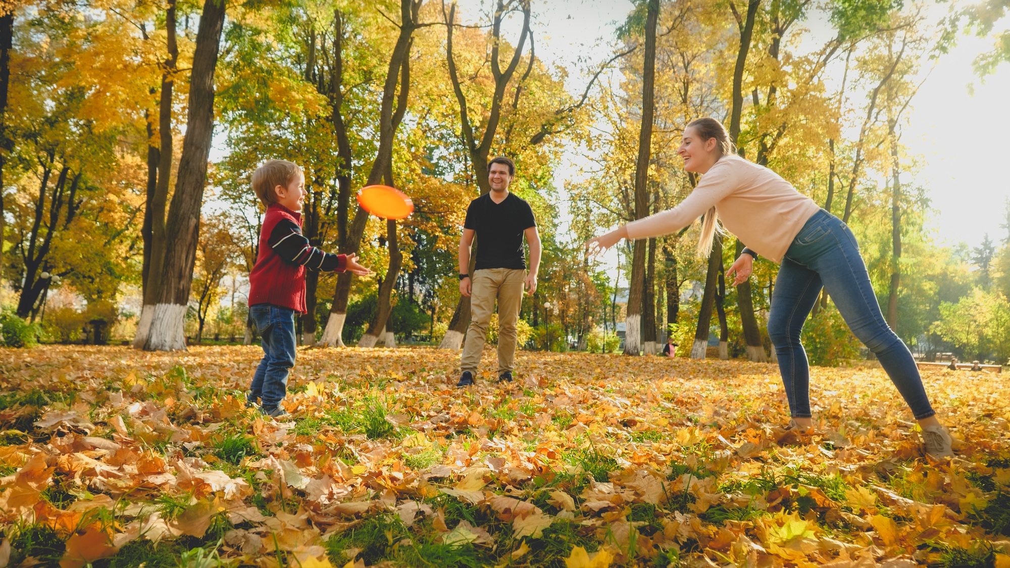 Beautiful young mother throwing frisbee to her little son at autumn park