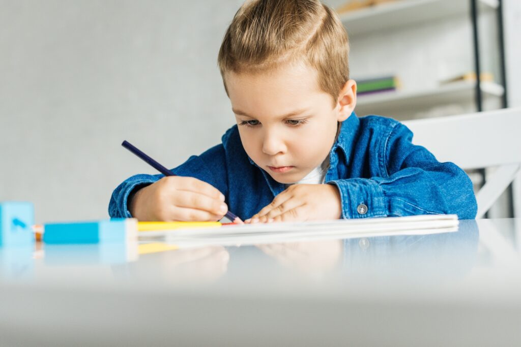 concentrated little kid drawing with color pencils at home