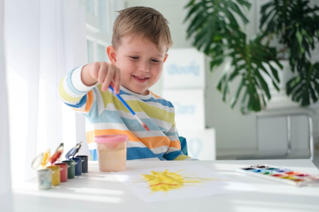 Happy kid painting with brush and colorful paints.