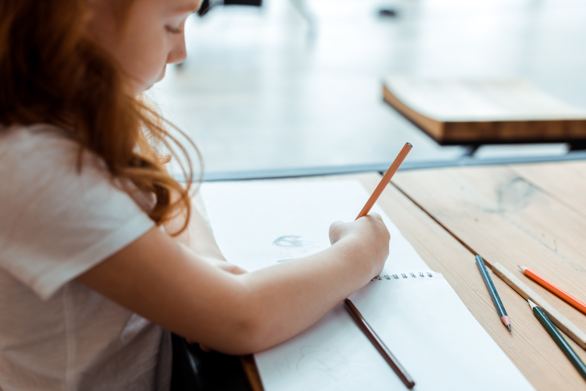 selective focus of redhead kid drawing on paper with color pencil
