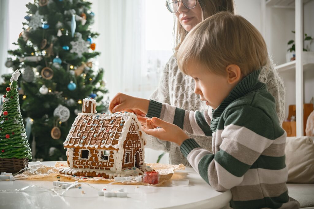 Little boy with mother decorating christmas gingerbread house together, family activities