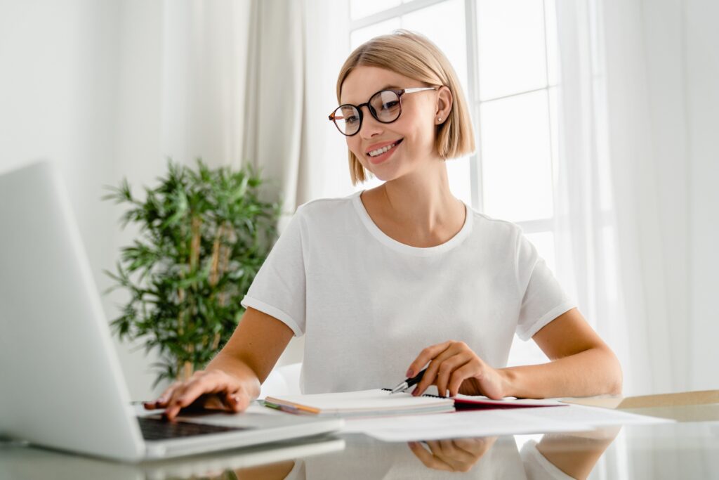 Young caucasian female freelancer using laptop for e-learning at home desk.