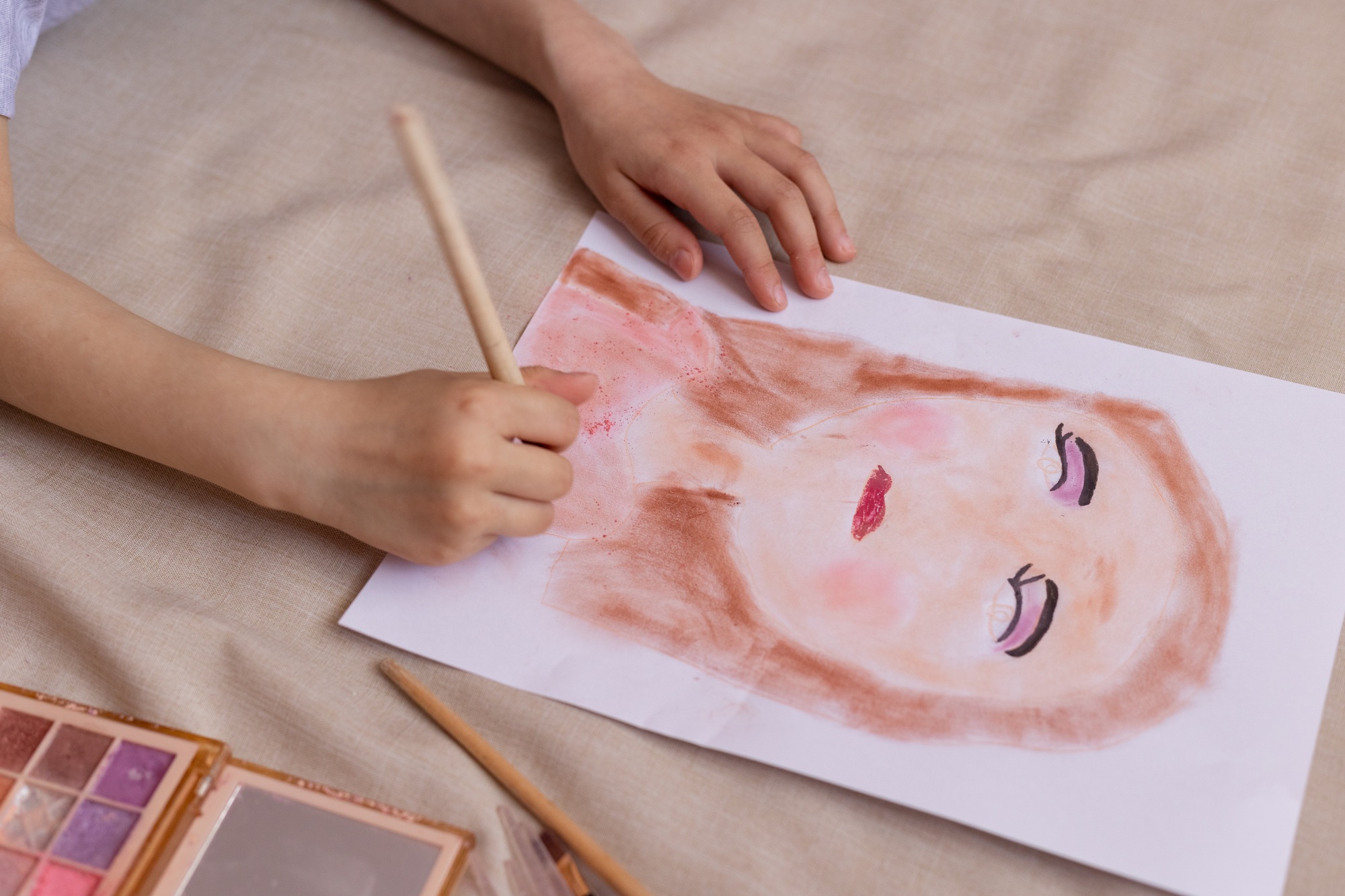A small child girl draws a portrait with her mother's cosmetics.