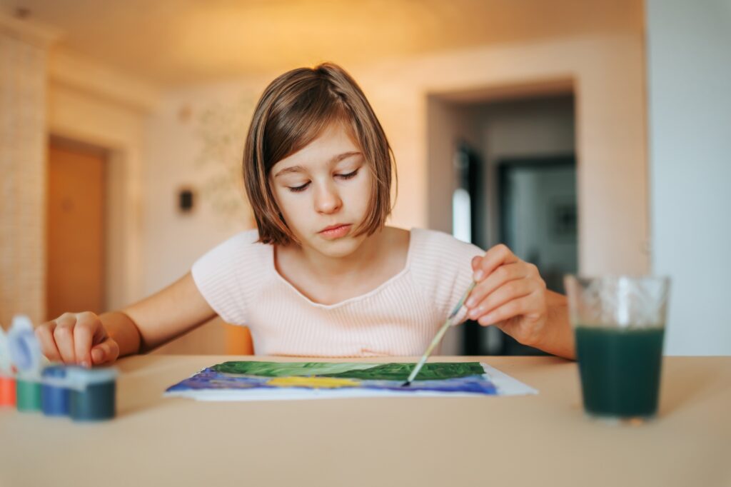 Serious beautiful concentrated girl sits at the table and draws, selective focus.